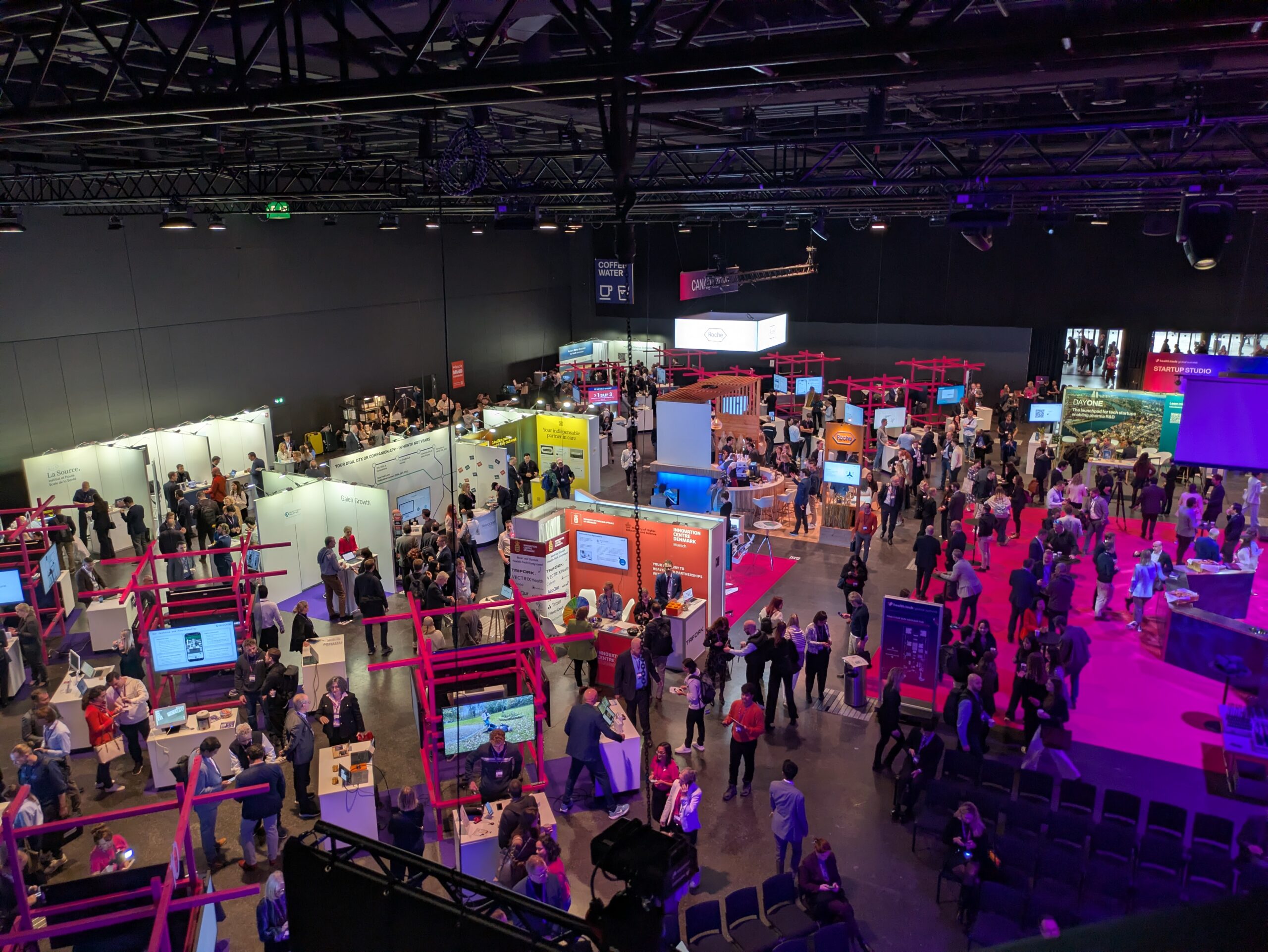 mage of the health.tech global summit venue in Basel that shows sponsor booths, startup stands, and one of the networking areas, buzzing with scientists, entrepreneurs, and investors.