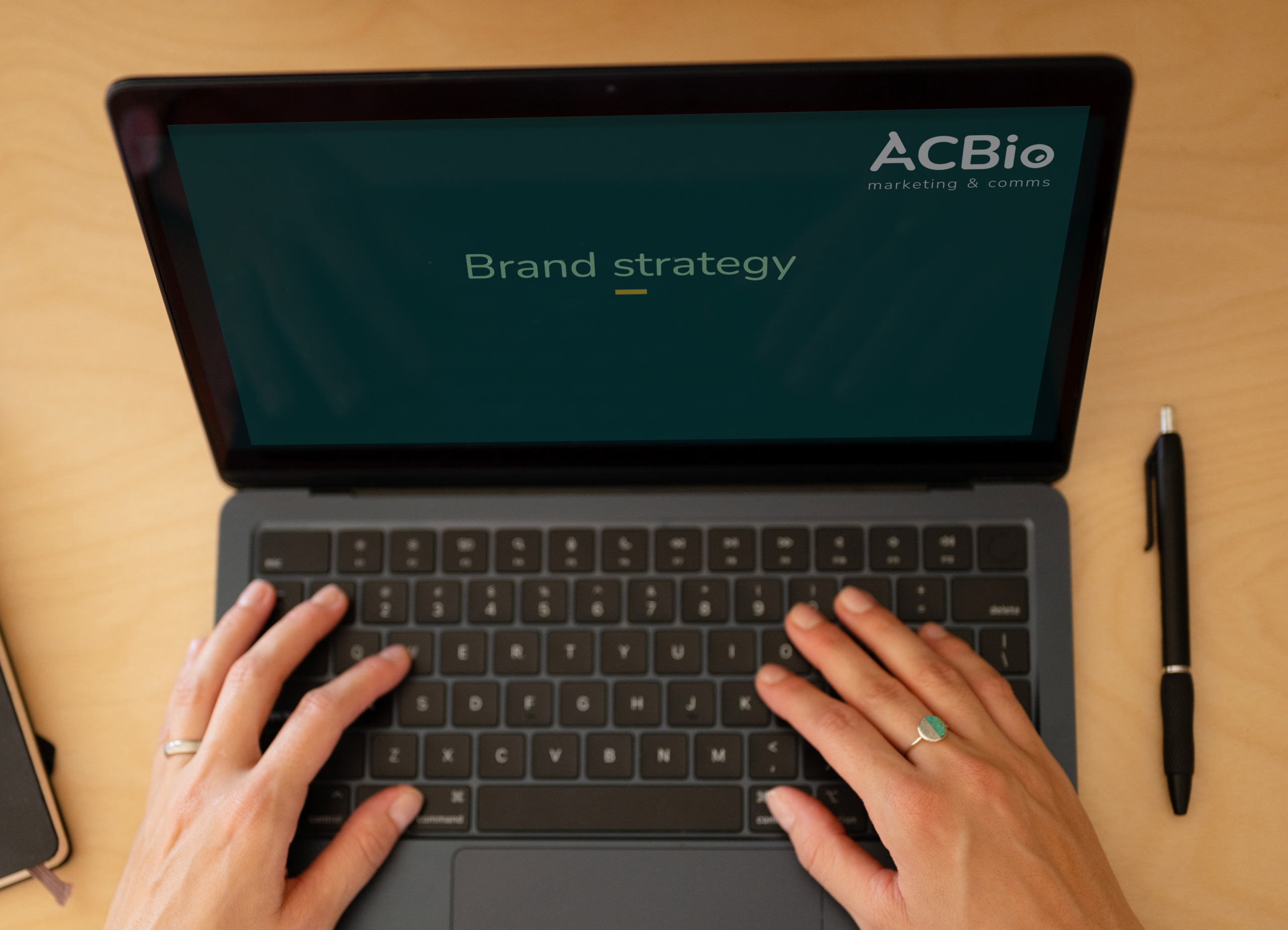Two hands typing on a laptop displaying a unified brand strategy blueprint and the ACBio logo for life science marketing.